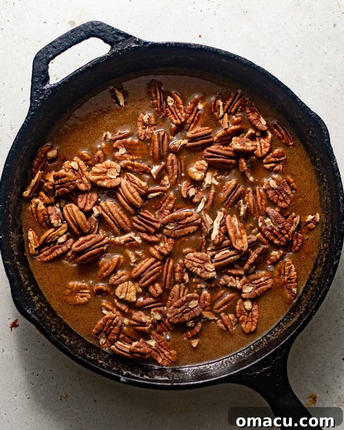 Chopped pecans carefully folded into the warm, gooey caramel sauce in a skillet, creating the luscious pecan pie filling.