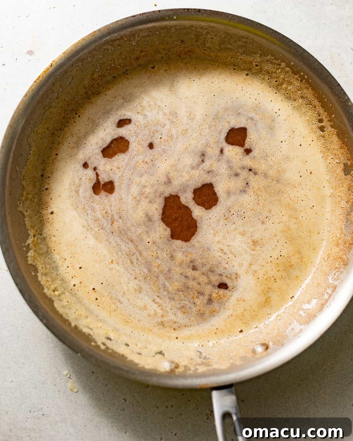 Perfectly browned butter in a skillet, ready to be strained for the pecan pie cheesecake crust.