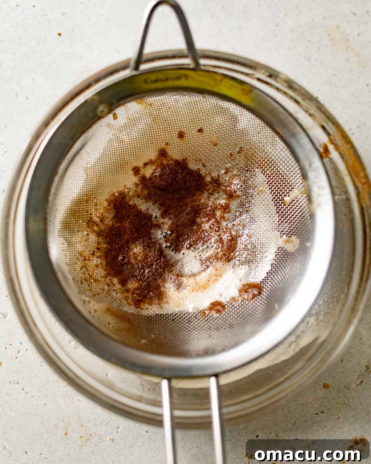 Straining browned butter through a fine-mesh sieve into a bowl, separating the liquid gold from the flavorful browned bits.