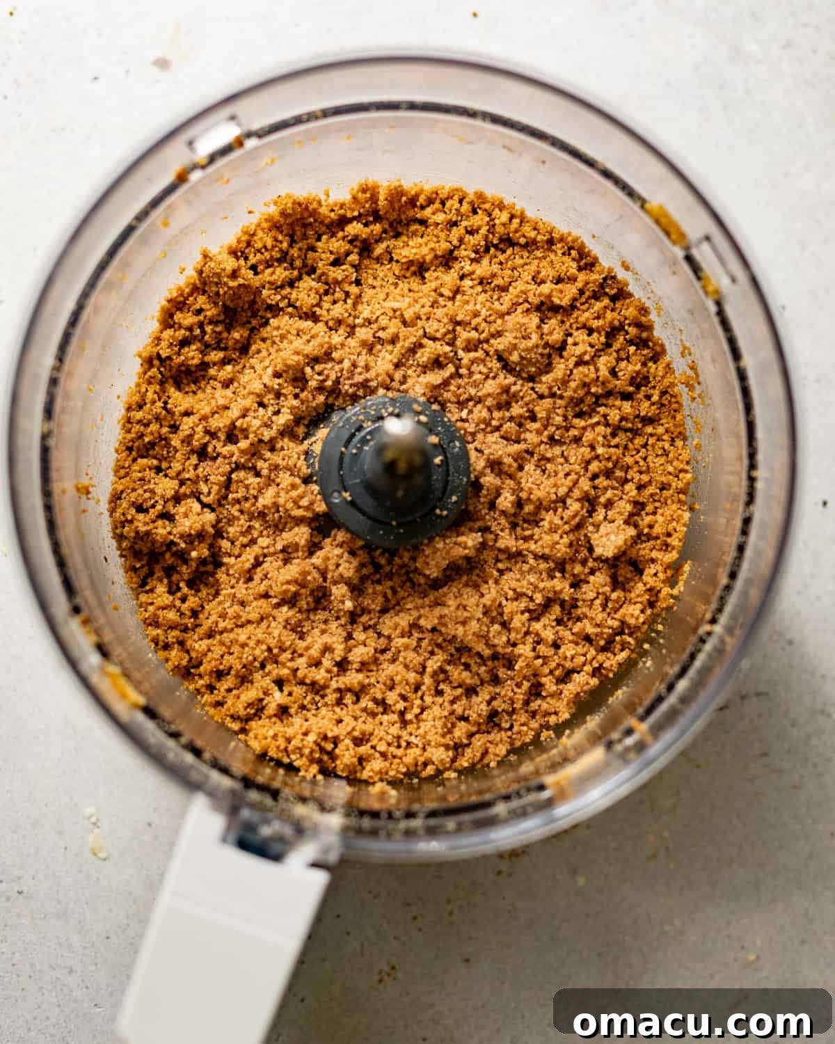 Graham cracker crumbs, toasted pecans, and other crust ingredients in a food processor, ready to be blended with brown butter.