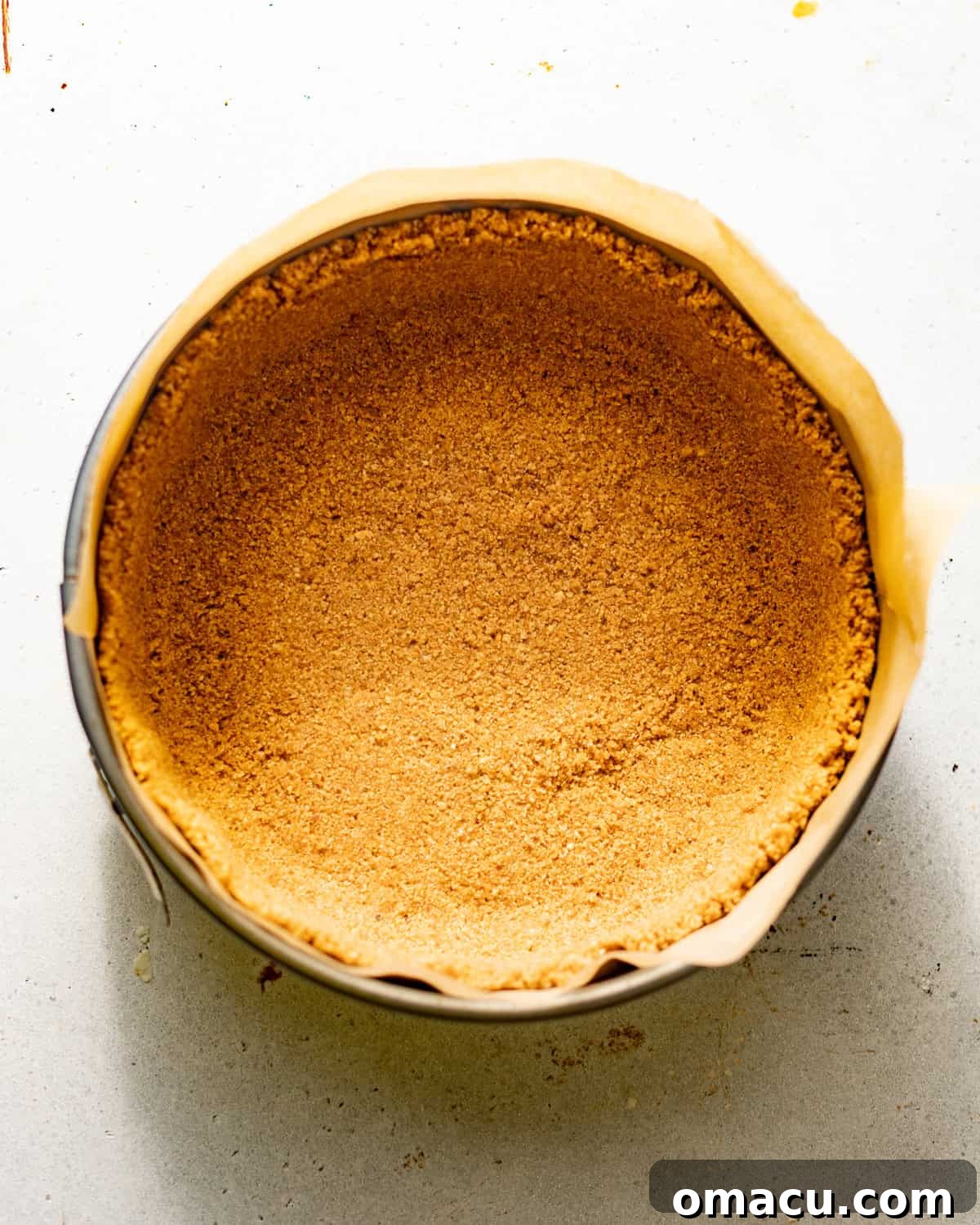 The brown butter pecan graham cracker crust firmly pressed into a parchment-lined springform pan, ready for baking.