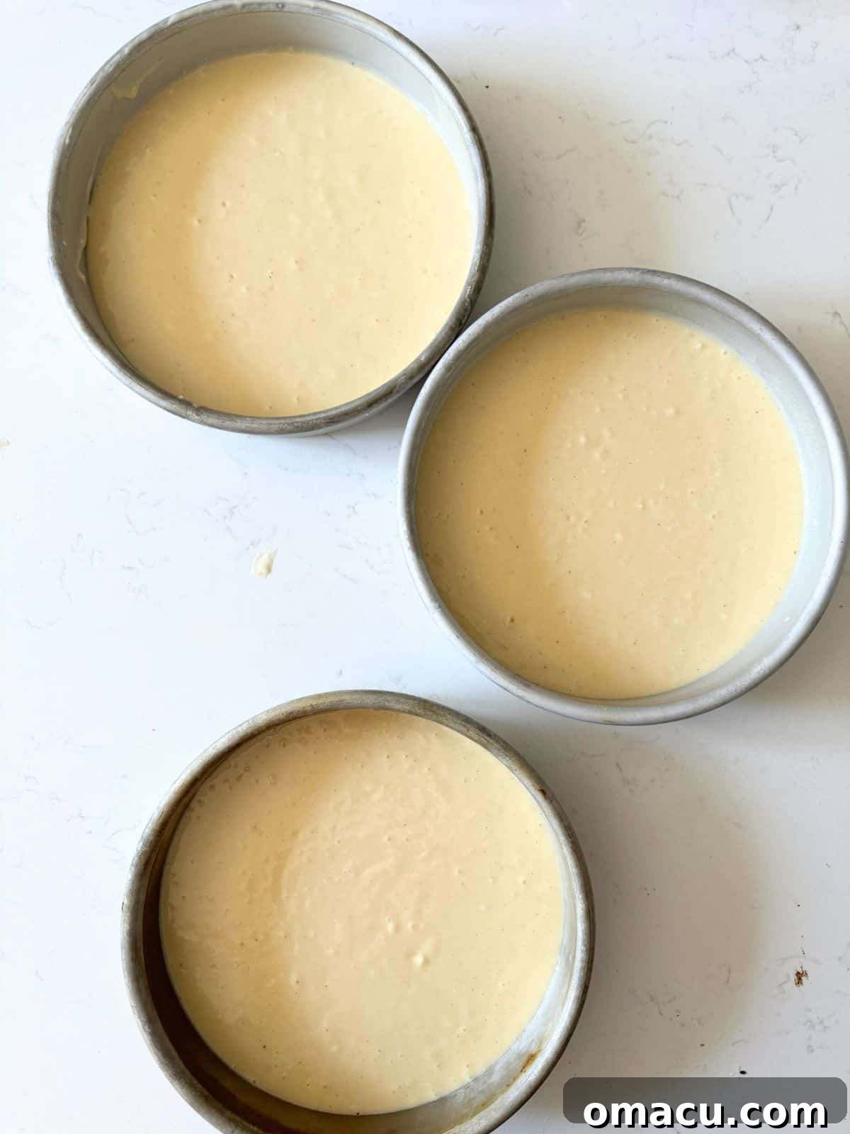 Yellow cake batter evenly divided into three 8-inch cake pans, ready for baking.