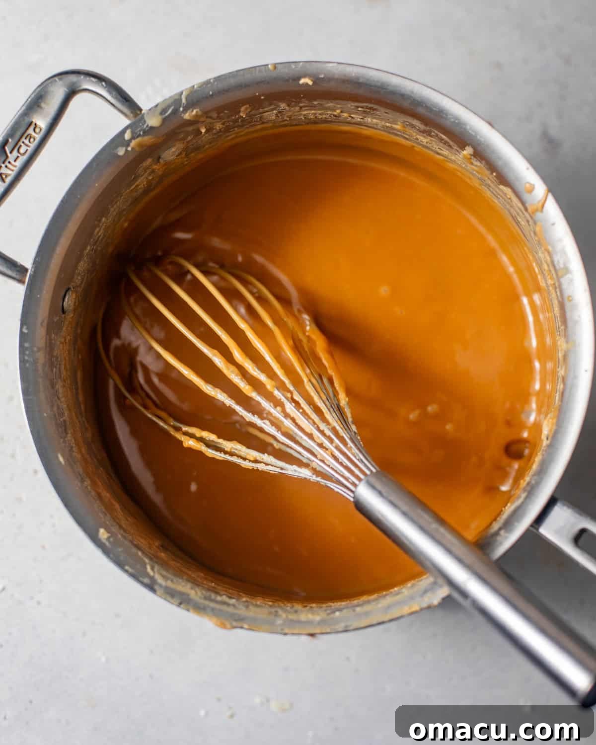 Caramel frosting mixture bubbling in a saucepan, being stirred with a whisk, showing its rich golden-brown color and thick consistency.