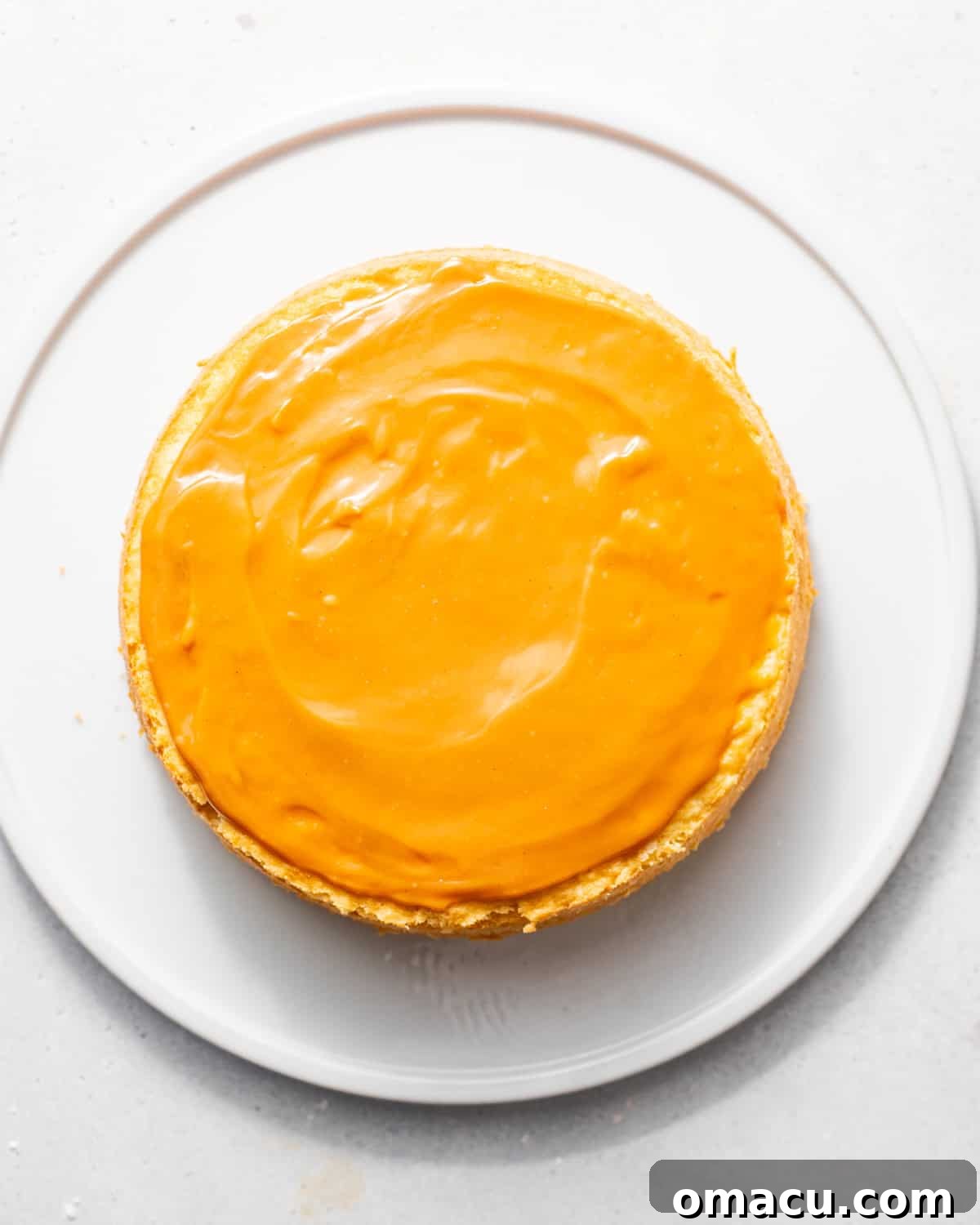 Warm caramel frosting being poured onto the first cooled cake layer on a cake stand, ready for assembly.