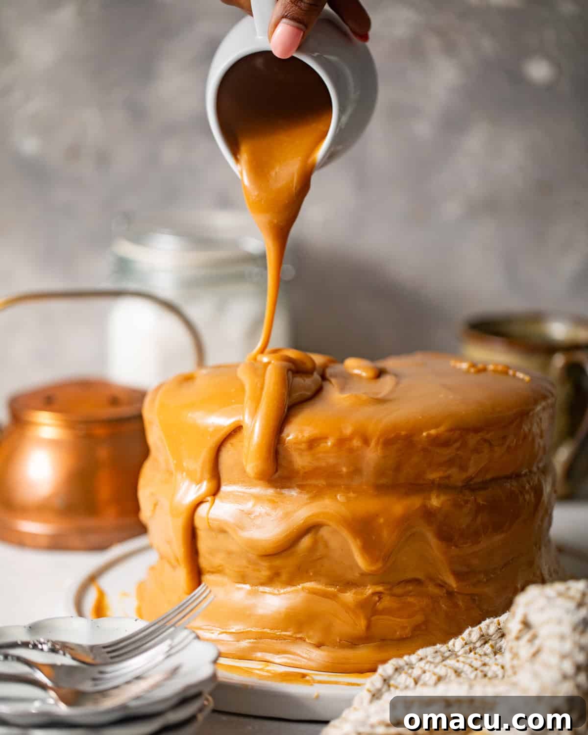 The final layer of yellow cake being topped with abundant caramel icing, smoothing it over the entire cake.