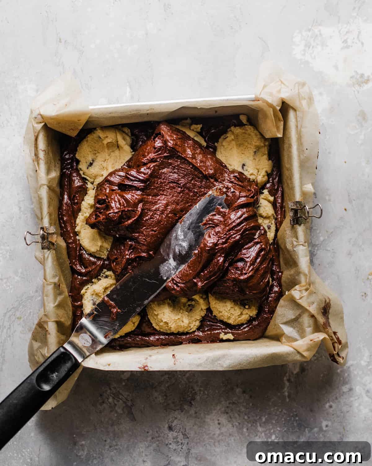 Half of the brownie batter spread in a baking pan, topped with a layer of chocolate chip cookie dough.