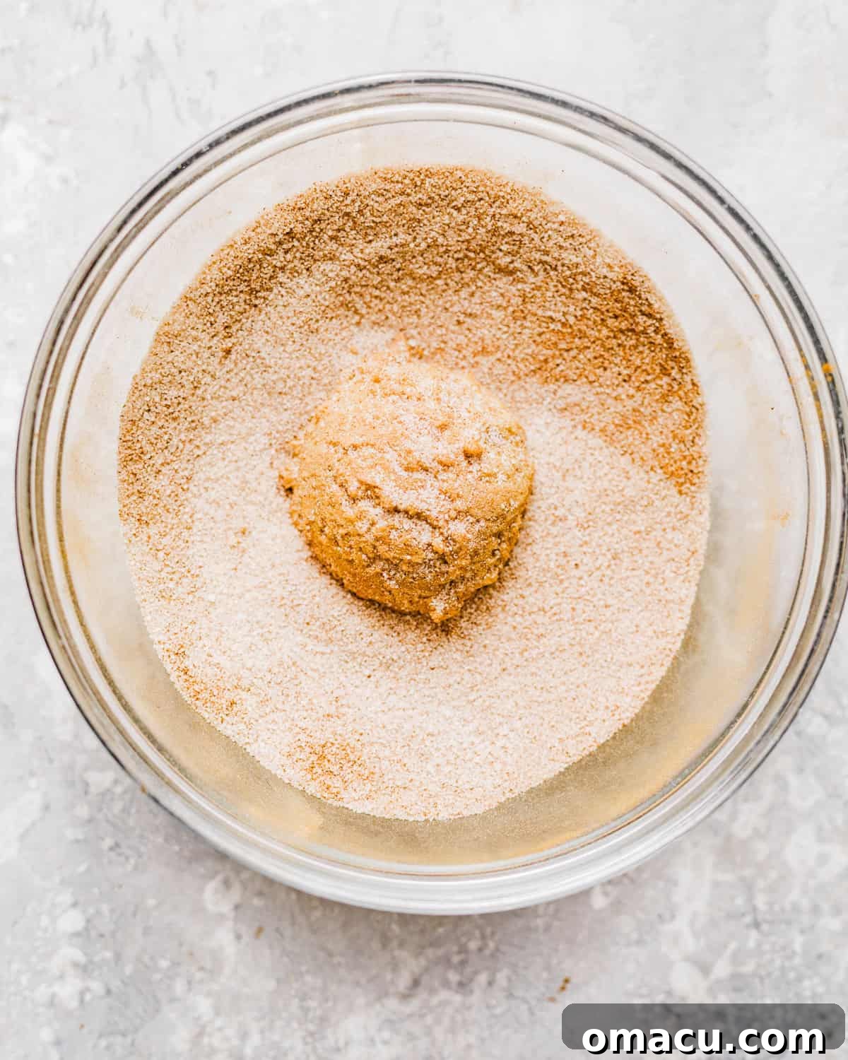 Cookie dough balls generously rolled in cinnamon sugar mixture on a baking sheet.