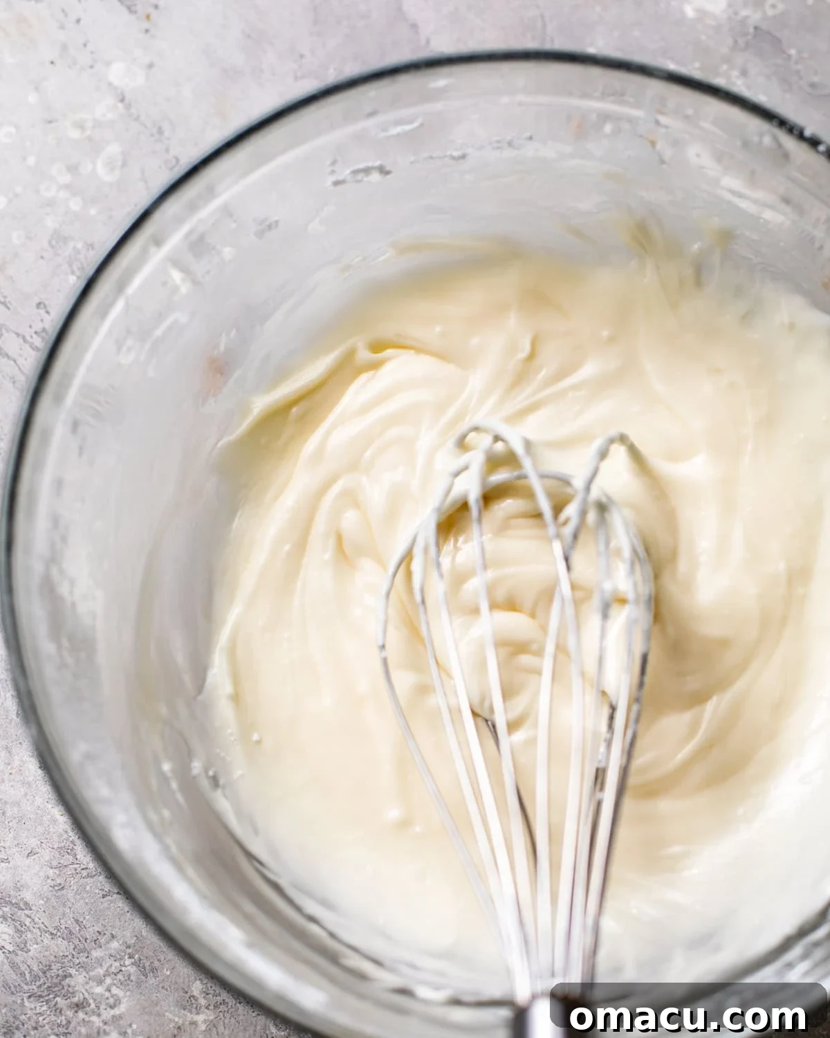 The ingredients for the spiced eggnog glaze, including melted butter, confectioner's sugar, eggnog, vanilla extract, rum extract, and ground nutmeg, are whisked together in a bowl until perfectly smooth and pourable.