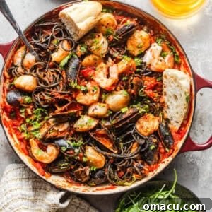 overhead photo of squid ink pasta with seafood in a pan with a side salad and a glass of white wine on the side.