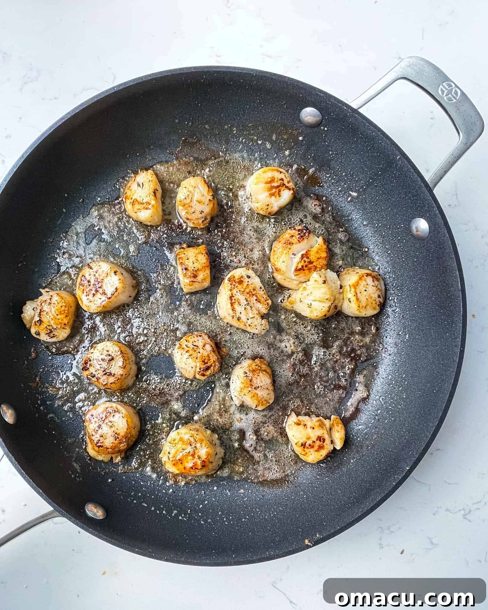 Seared golden-brown scallops cooking in a hot skillet, showing their caramelized edges.