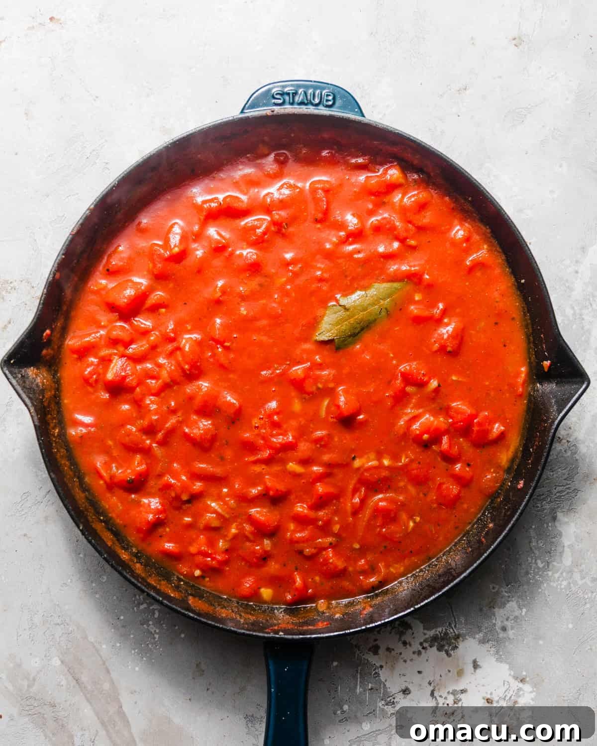 A rich tomato and white wine sauce simmering in a skillet with a bay leaf, ready for mussels to be added.