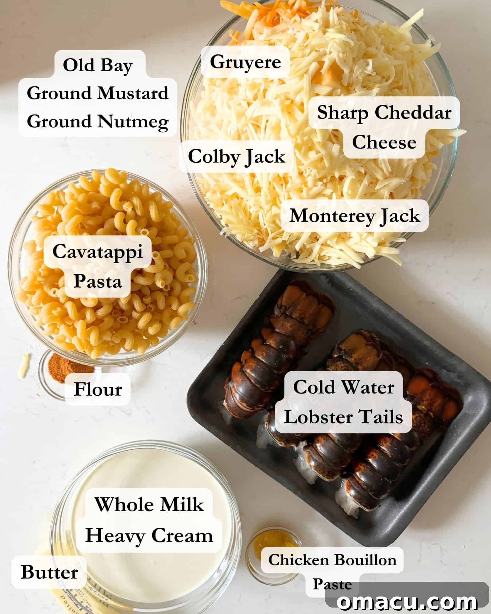 ingredients to make lobster mac and cheese on a white counter top in bowls - colby jack, gruyere cheese, monterey jack cheese, sharp cheddar cheese, lobster tails, pasta, seasonings, heavy cream, and whole milk