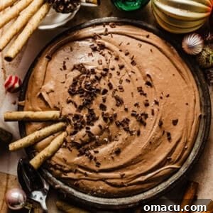 Hot cocoa dip in a festive serving bowl with chocolate shavings on top, surrounded by cheerful Christmas ornaments, highlighting its holiday appeal.