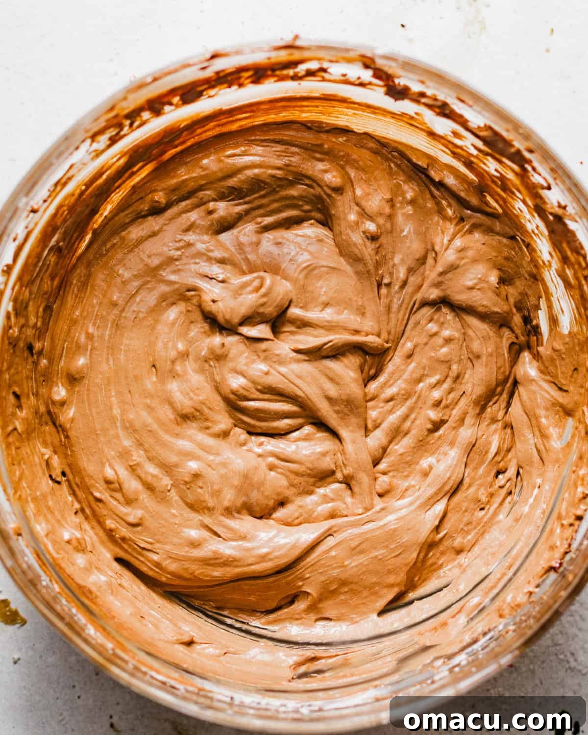 The fluffy whipped cream mixture being gently folded into the rich chocolate base in a large mixing bowl using a spatula, ensuring the two components are smoothly and evenly combined to create the final hot cocoa dip.