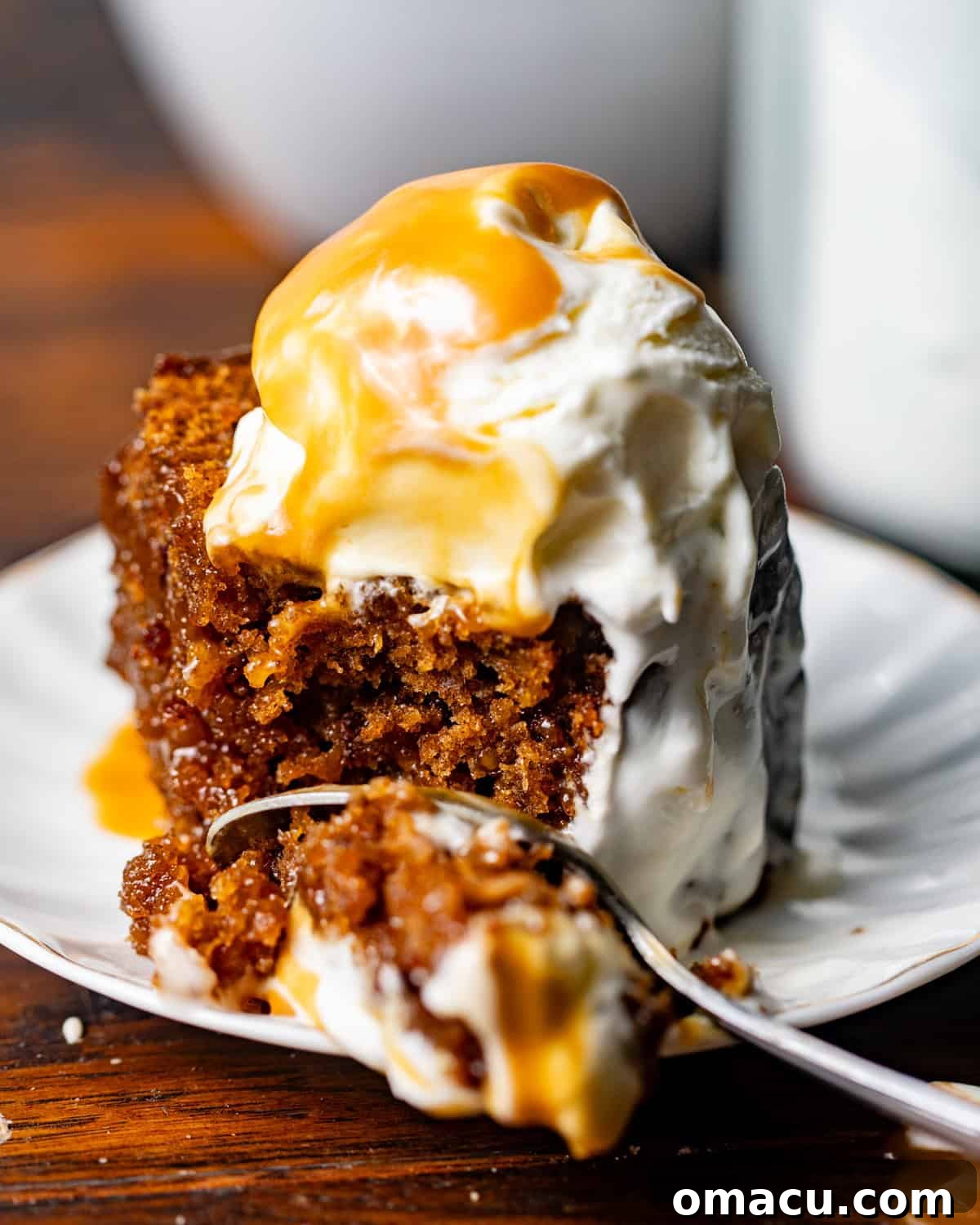 A spoon scooping sticky toffee pudding cake with toffee sauce and ice cream melting into the cake.