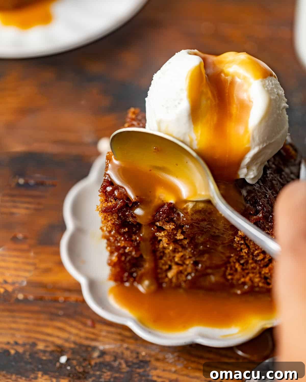 Up close photo of sticky toffee pudding on a plate with a spoon scooping a piece of cake.