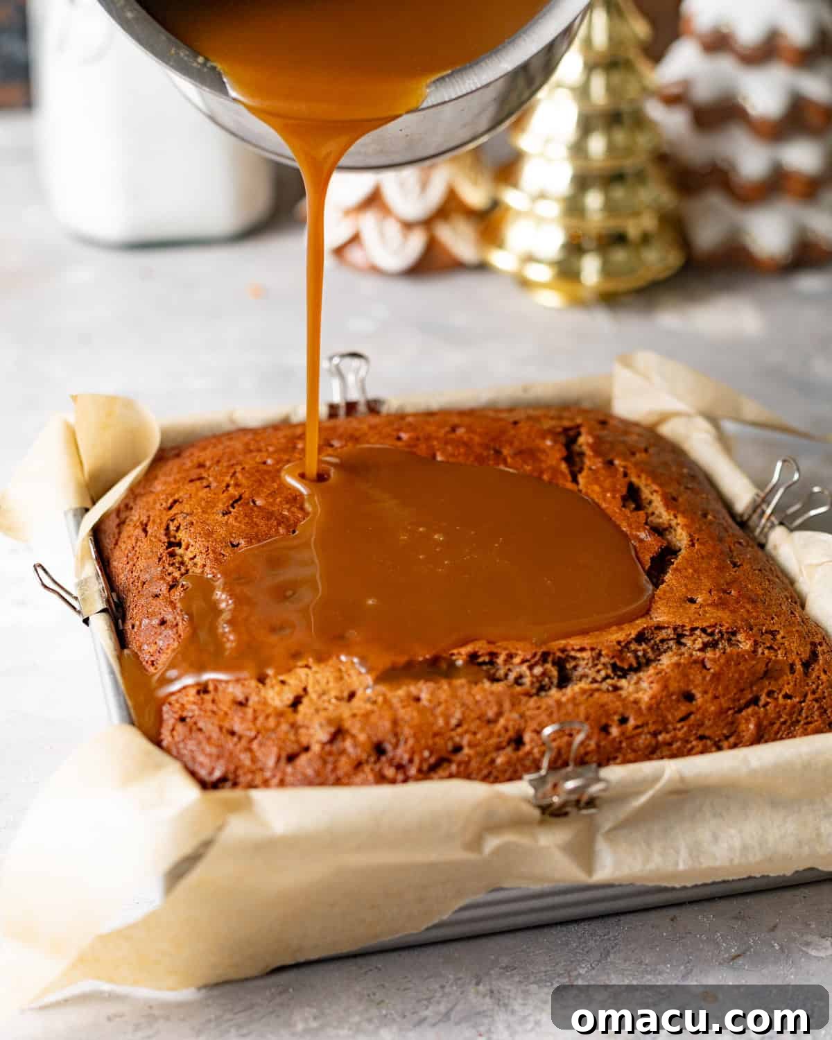 Baked sticky toffee pudding with toffee sauce being poured on top after baking.