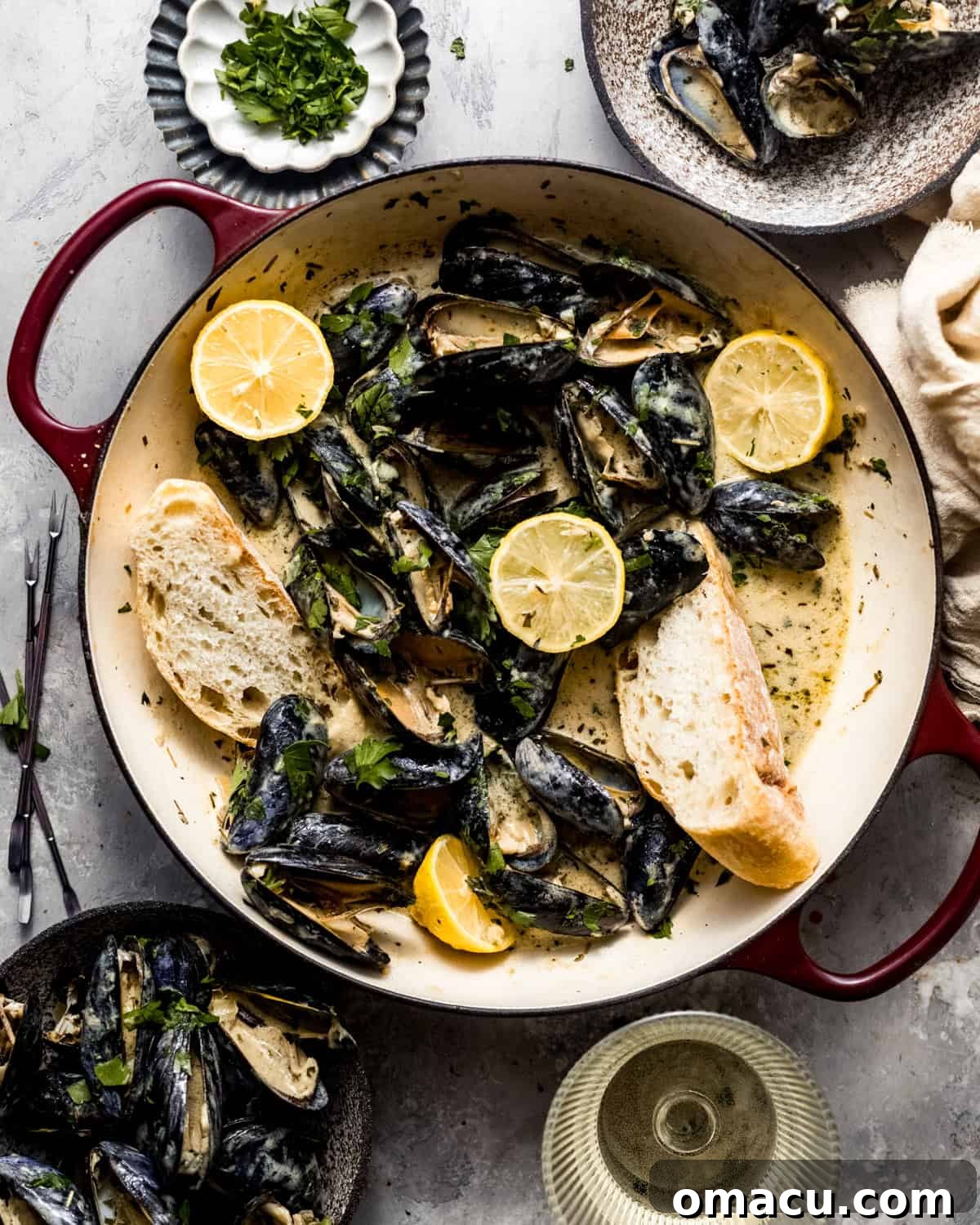 Mussels in white wine sauce served in a pan with crusty bread, fresh lemons, and parsley as garnish.
