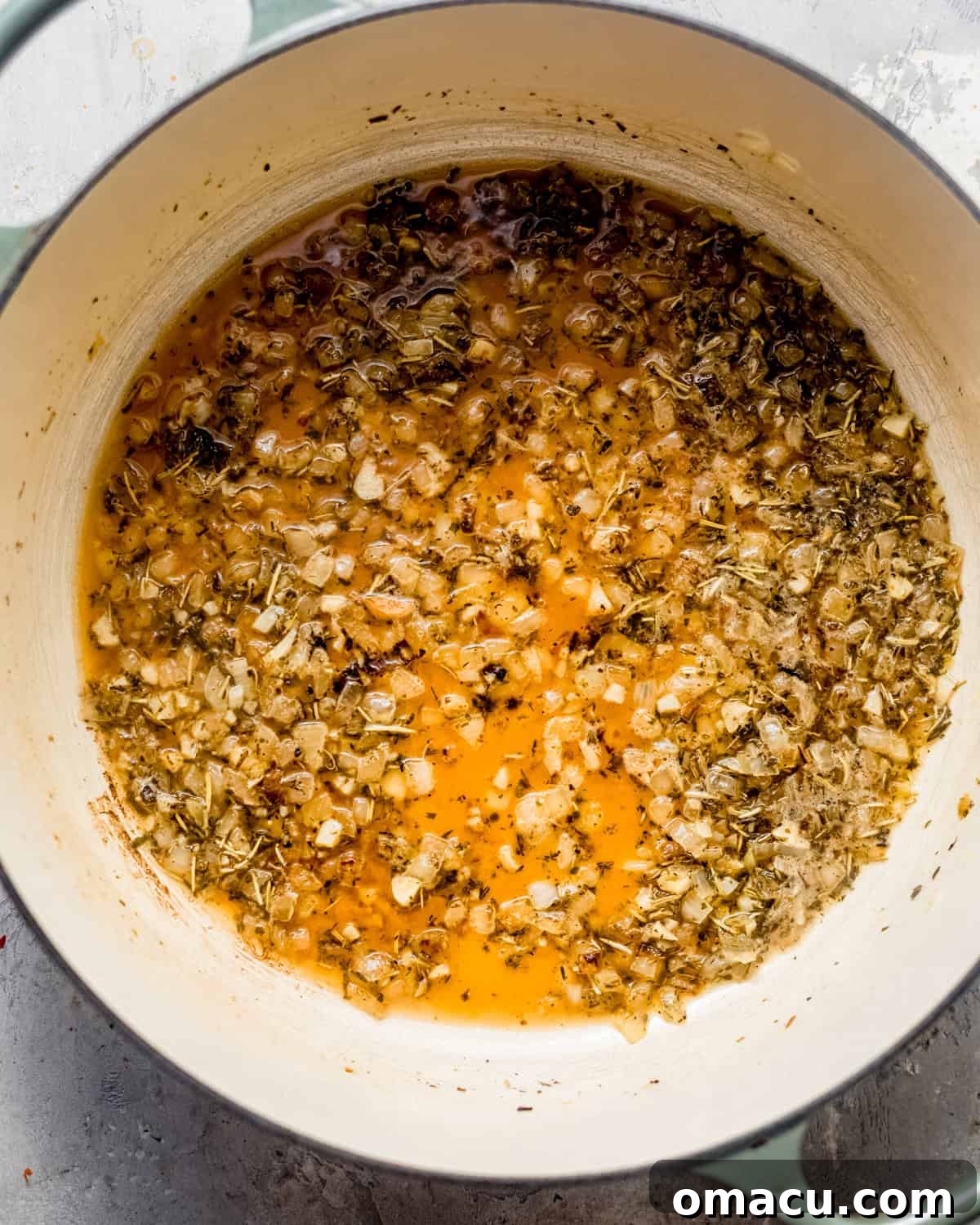 Olive oil, shallots, garlic, herbs de provence, white wine, and chicken broth simmering in a pan.