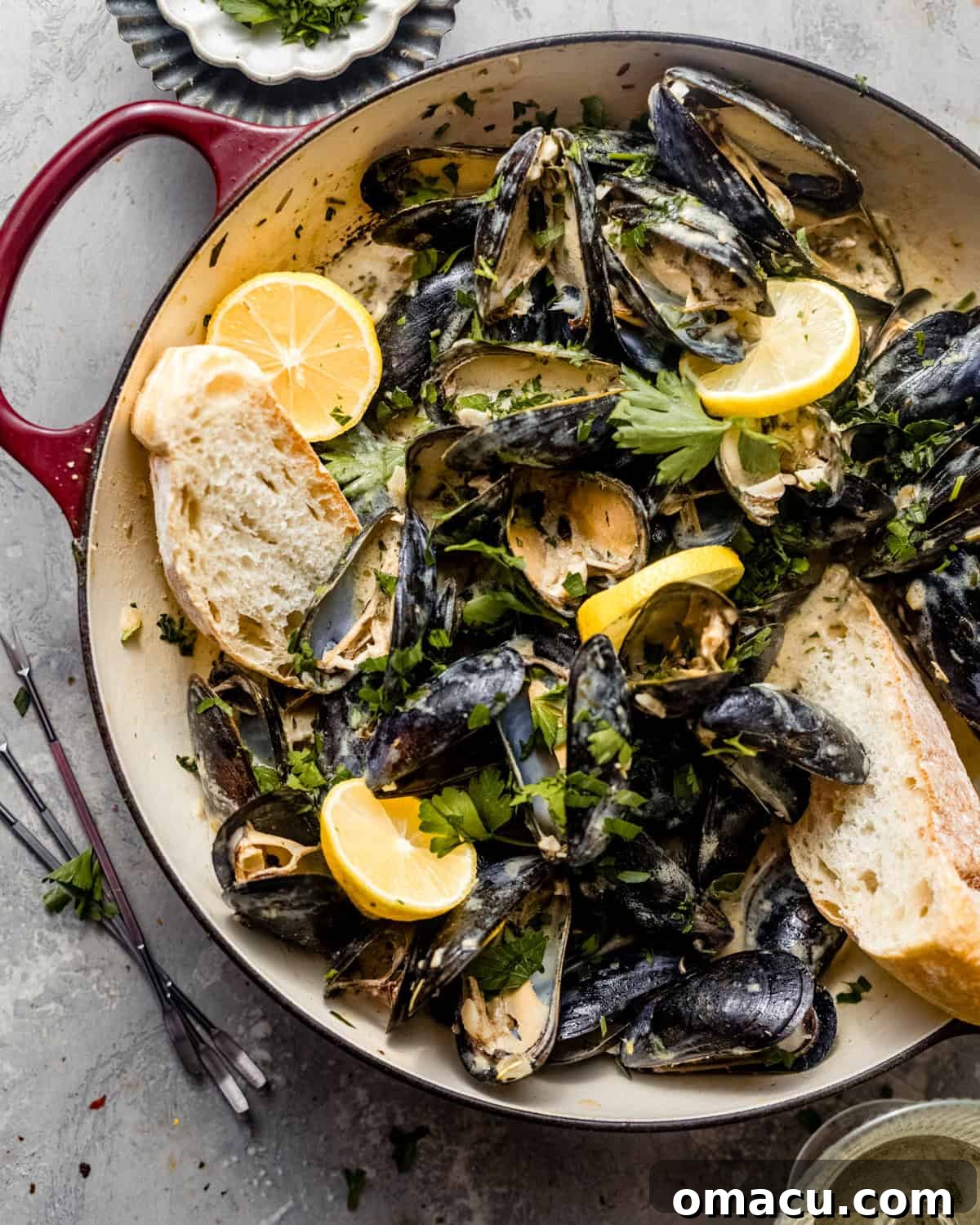 Finished mussels in a pan served with crusty bread and lemon wedges on the side, garnished with parsley.