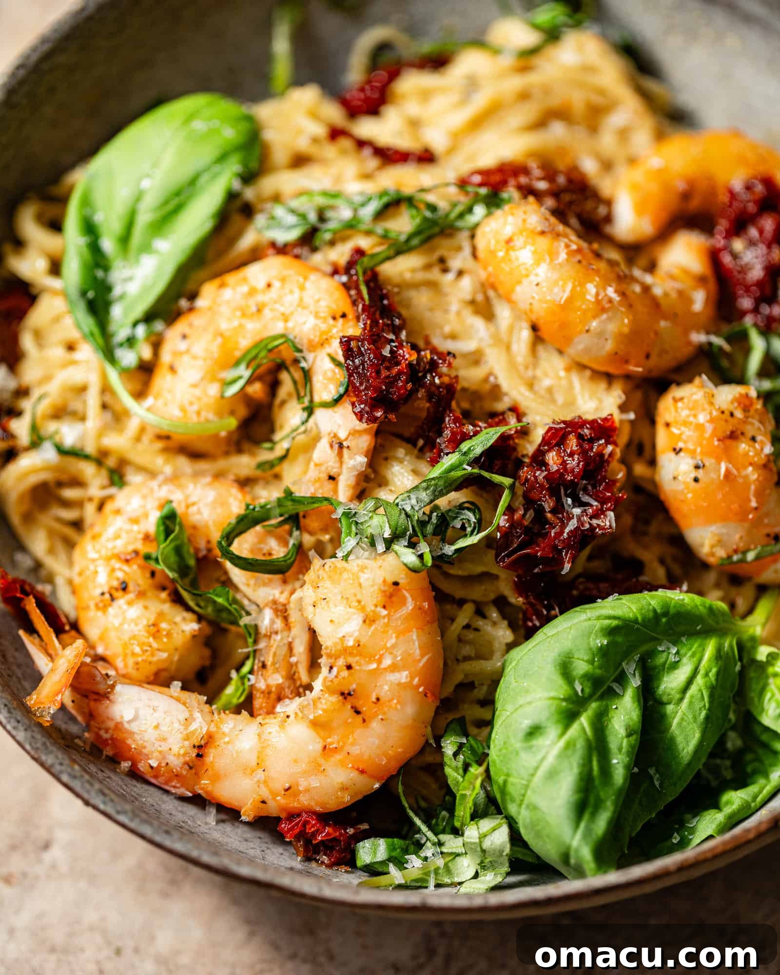 Close-up photo of delicious pesto shrimp pasta in a bowl, showing the creamy sauce, sun-dried tomatoes, and fresh basil garnish.