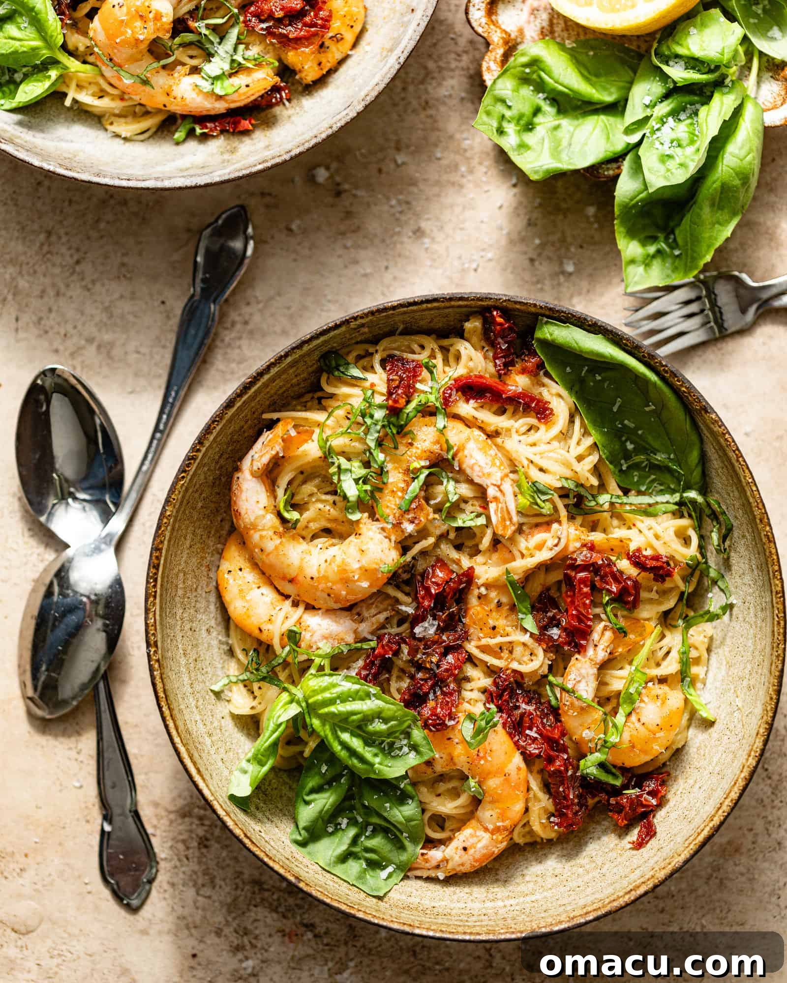 Two bowls of pesto shrimp pasta artfully arranged on a table, garnished with fresh basil, forks and spoons nearby.