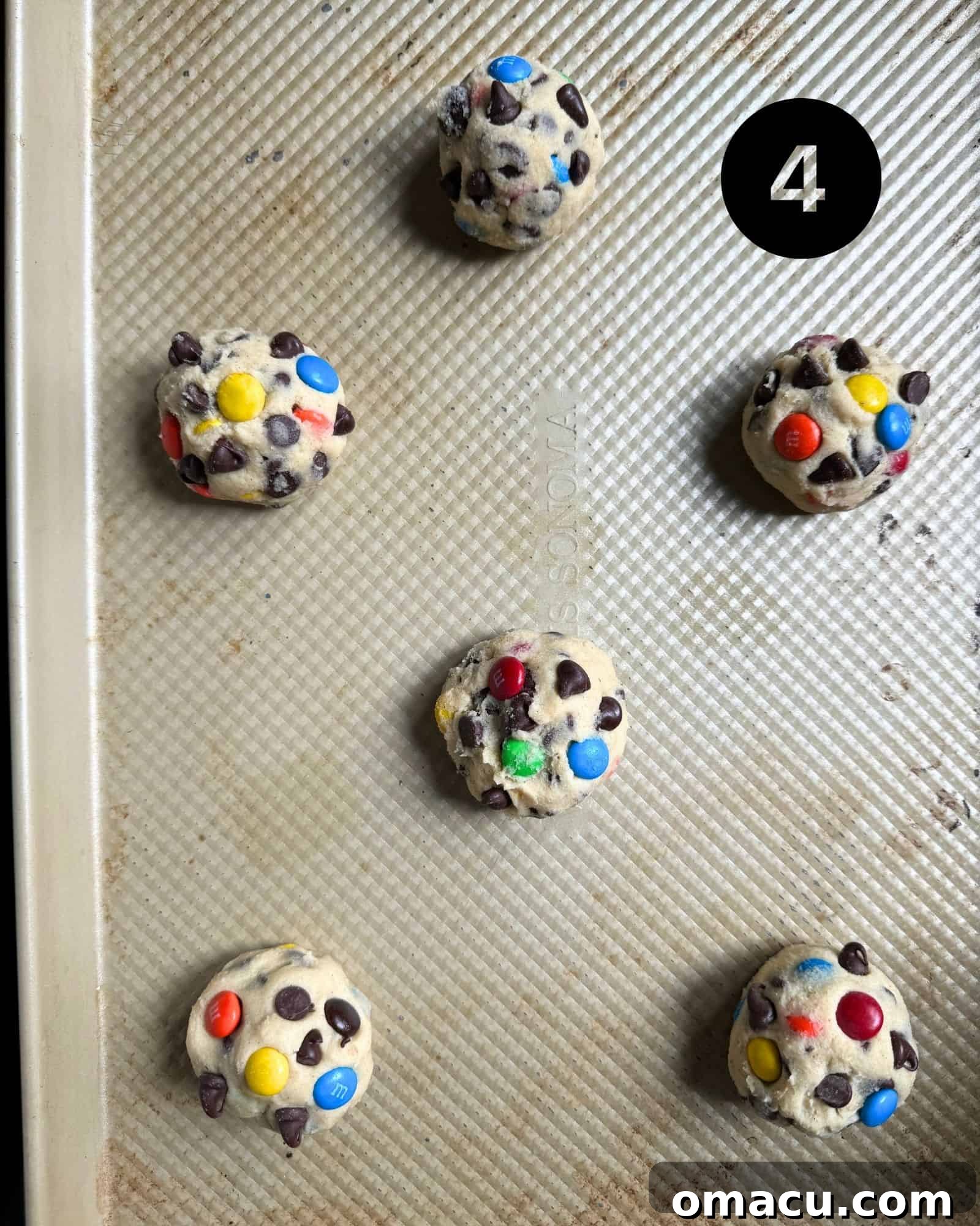 Portioned cookie dough balls, topped with extra M&Ms, arranged on a baking sheet lined with parchment paper.