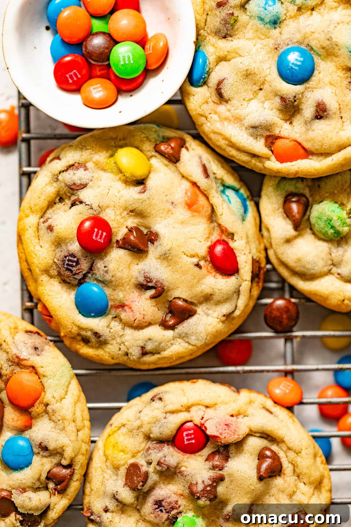 A close-up view of freshly baked M&M chocolate chip cookies cooling on a wire rack, showcasing their vibrant colors and perfect texture.