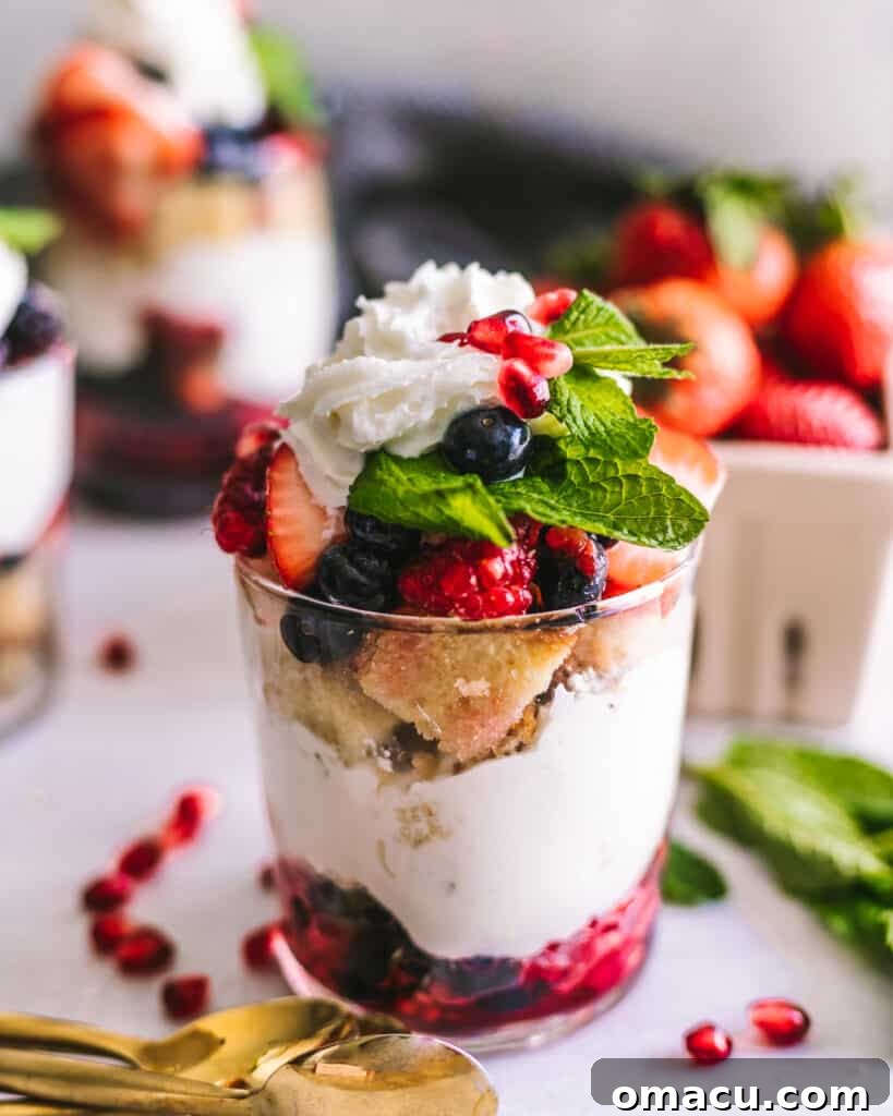 Close-up shot of Mixed Berry Trifles in clear cups, showcasing the distinct layers of cake, berries, and whipped cream, with spoons nearby.