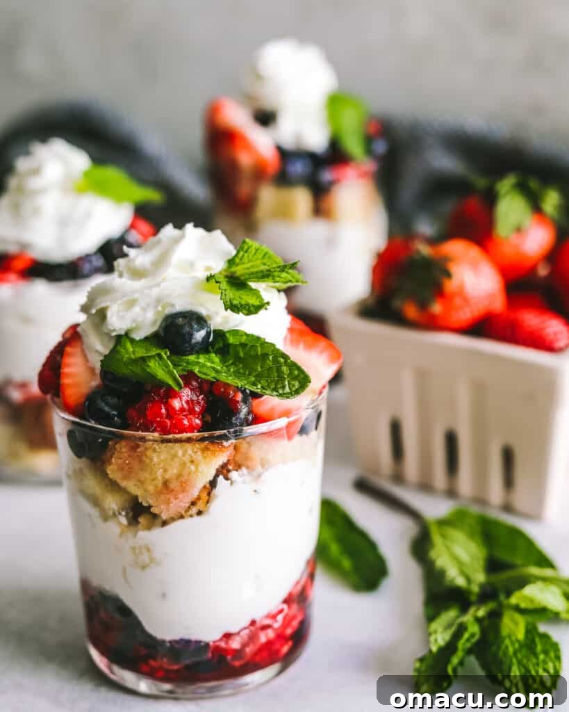 Individual Mixed Berry Trifles in clear glasses, garnished with whole berries and a mint leaf, photographed from a slightly elevated angle.