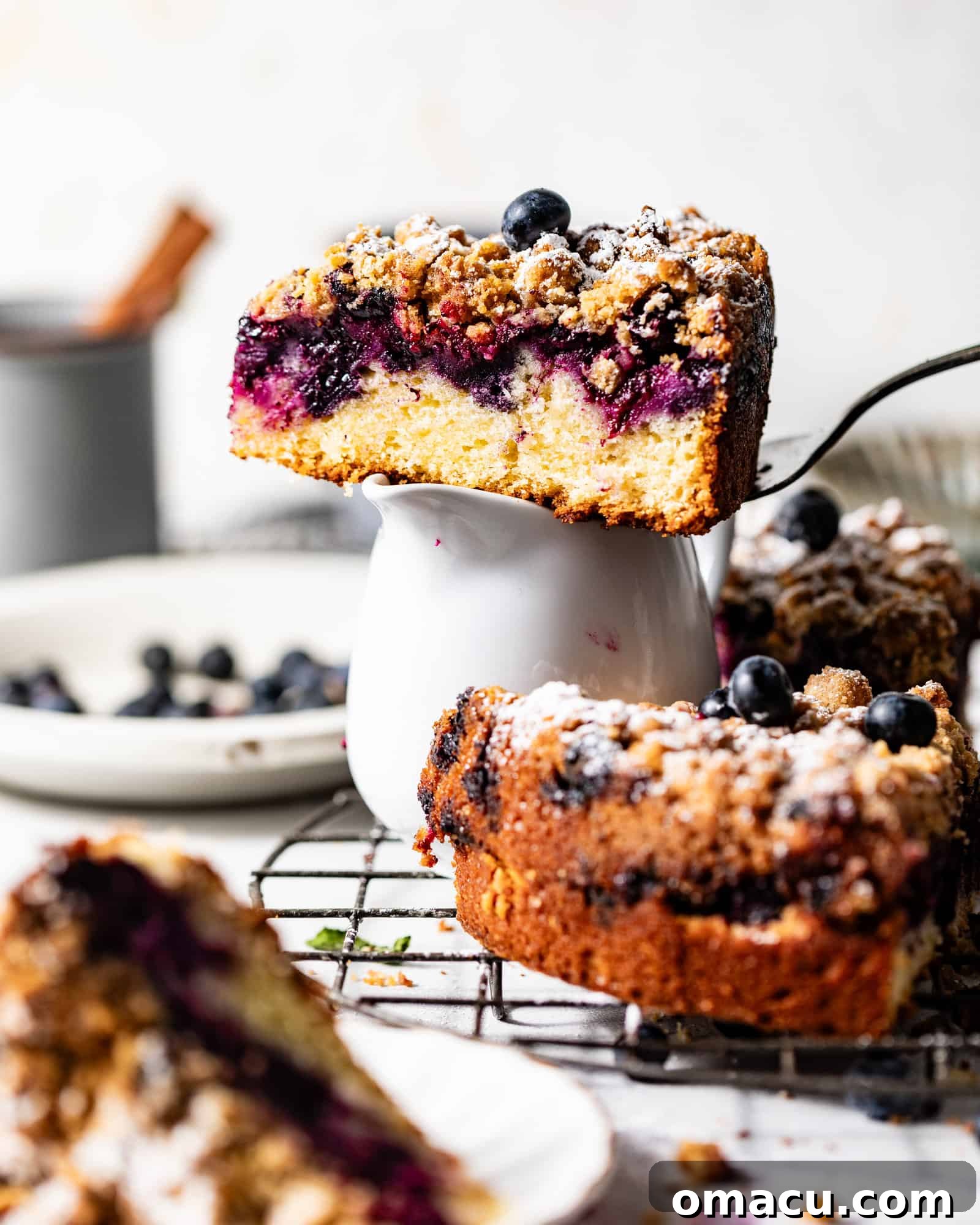 A slice of blueberry sour cream coffee cake elegantly presented on a cake server, balanced atop a coffee cup.