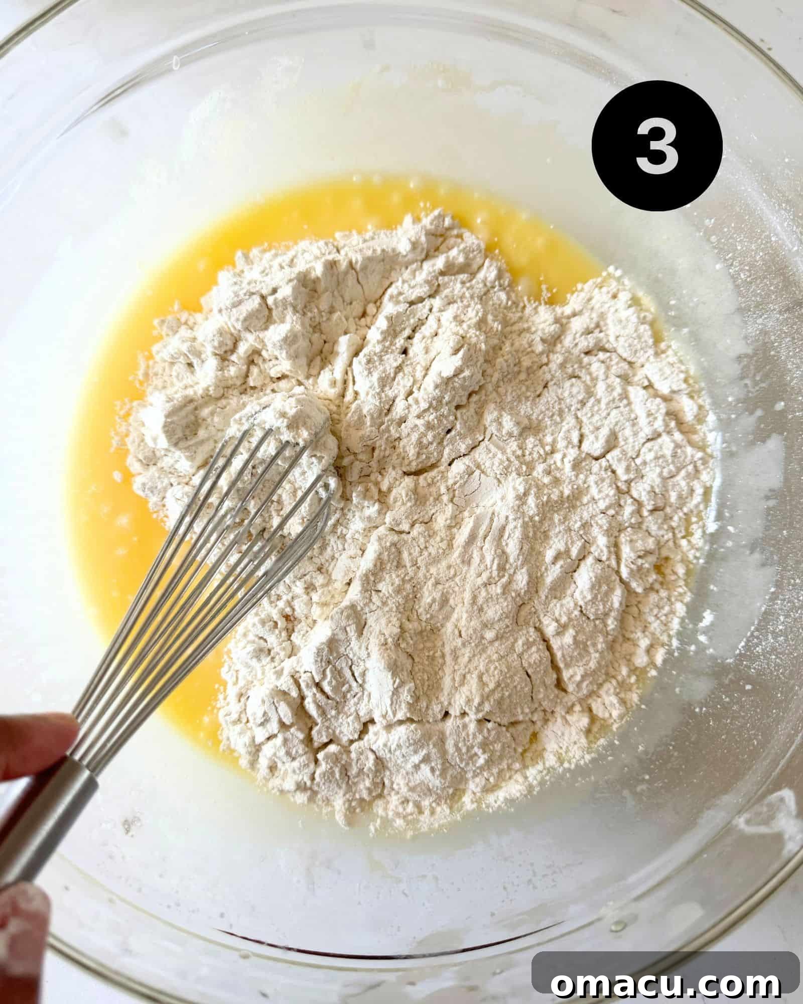 A bowl showing the wet and dry ingredients just combined into a smooth coffee cake batter, being mixed with a whisk.
