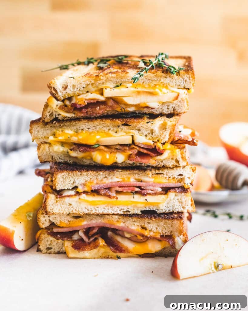Apple Bacon Cheddar Grilled Cheese, perfectly cut in half and stacked, showcasing melted cheese and crisp ingredients.