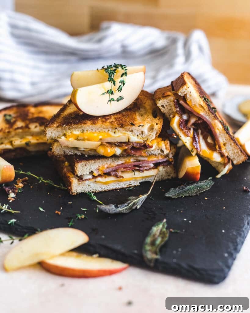 Apple Bacon Cheddar Grilled Cheese, halved and presented artfully on a plate.