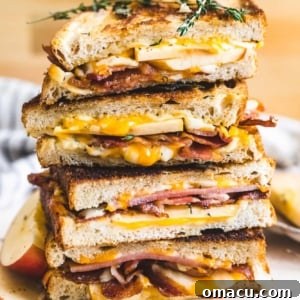 An apple bacon grilled cheese sandwich cut in half and stacked on top of each other with the cheese oozing out of the sandwich.