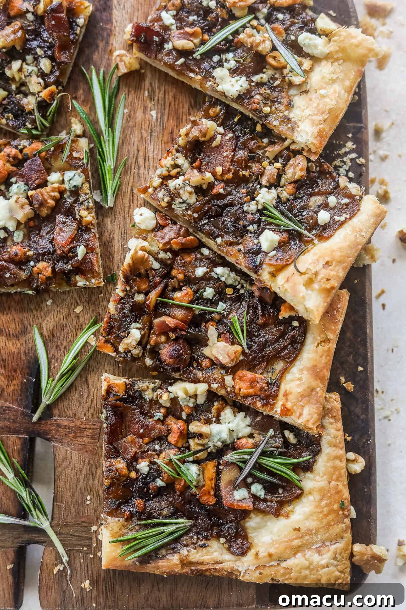 Gourmet Caramelized Onion Puff Pastry with bacon and gorgonzola, garnished with fresh rosemary, on a rustic cutting board.