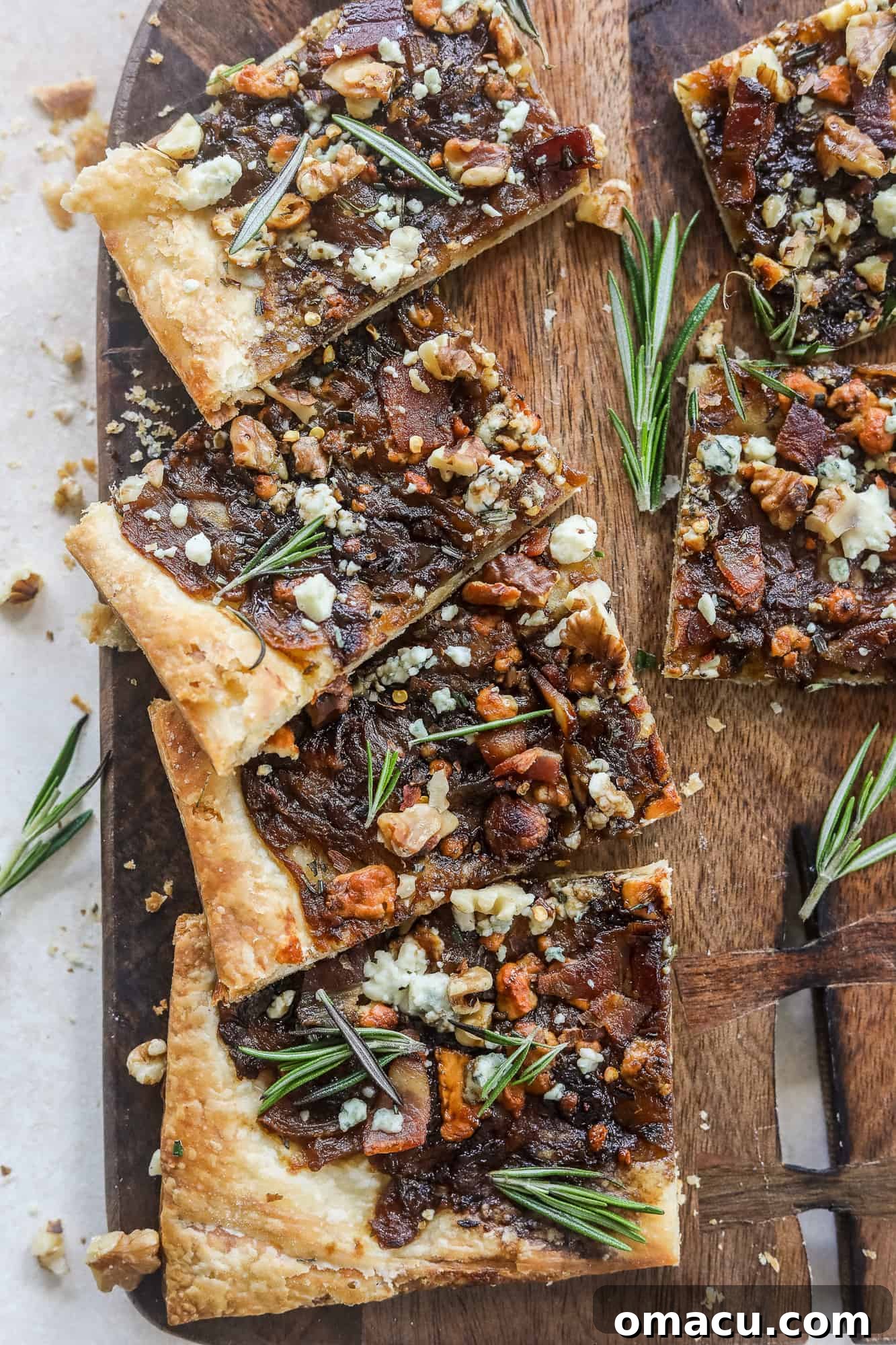 A freshly baked Caramelized Onion Puff Pastry with bacon and gorgonzola, glistening with balsamic glaze, on a wooden board.