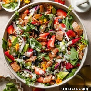A vibrant strawberry pecan salad in a serving bowl, elegantly topped with poppyseed dressing, surrounded by plates and a small bowl, indicating it's ready for dining.