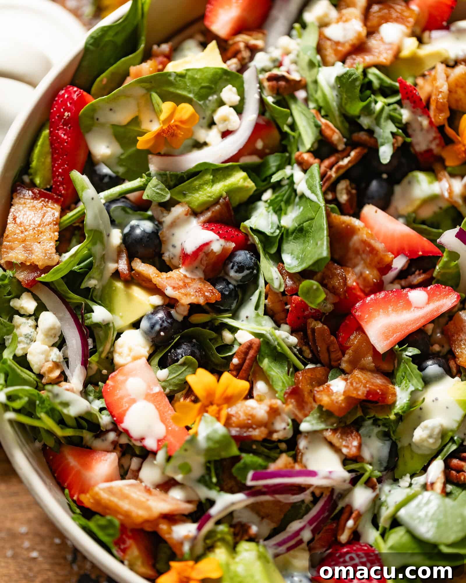 A vibrant assortment of fresh ingredients for strawberry pecan salad displayed in a large bowl, including bright red strawberries, deep green spinach and arugula, plump blueberries, crispy bacon, rich gorgonzola cheese, creamy avocado slices, and crunchy candied pecans.