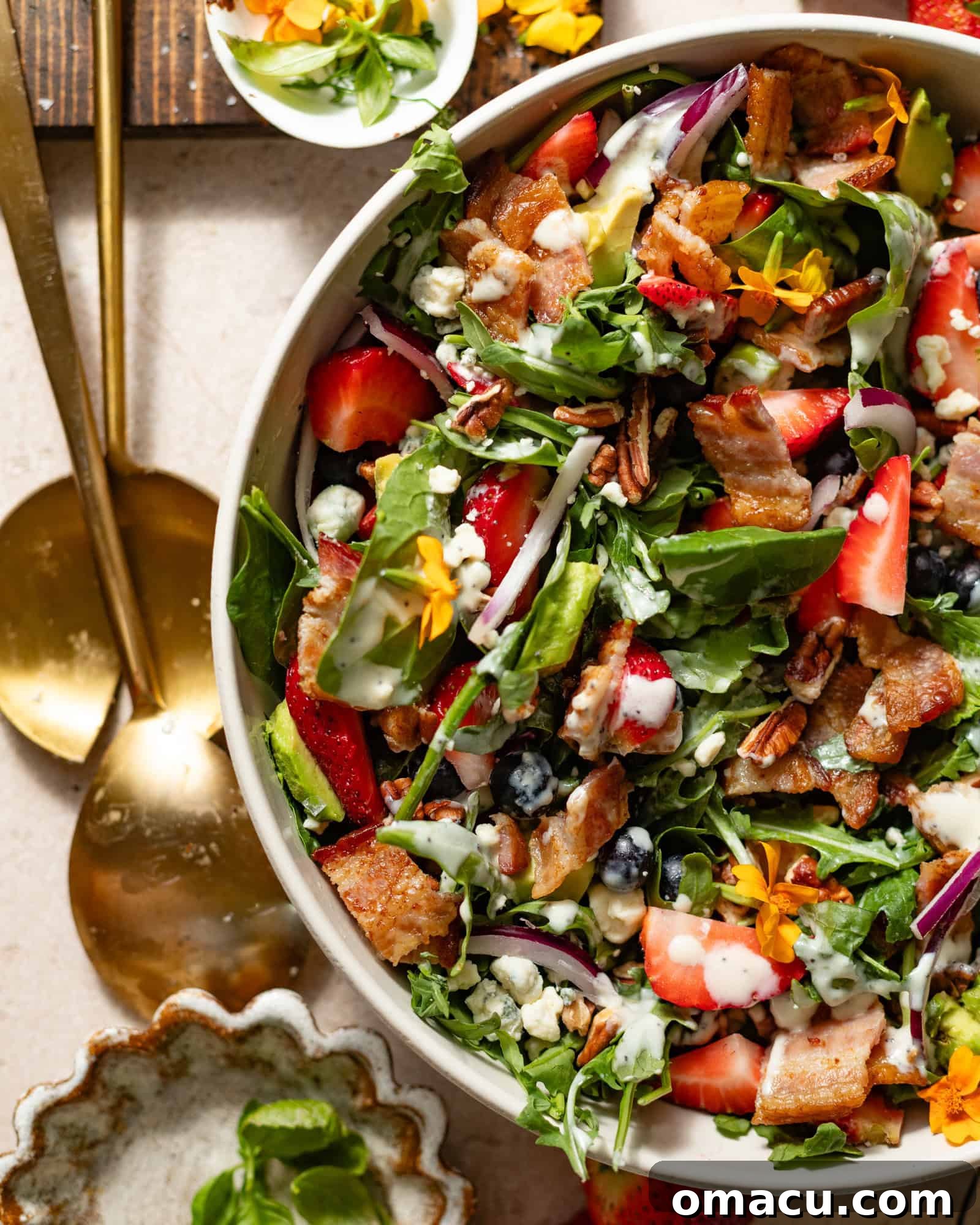 A beautifully presented strawberry blueberry spinach salad in a large elegant bowl, accompanied by two stylish salad forks on a serving board, ready for a delightful meal.