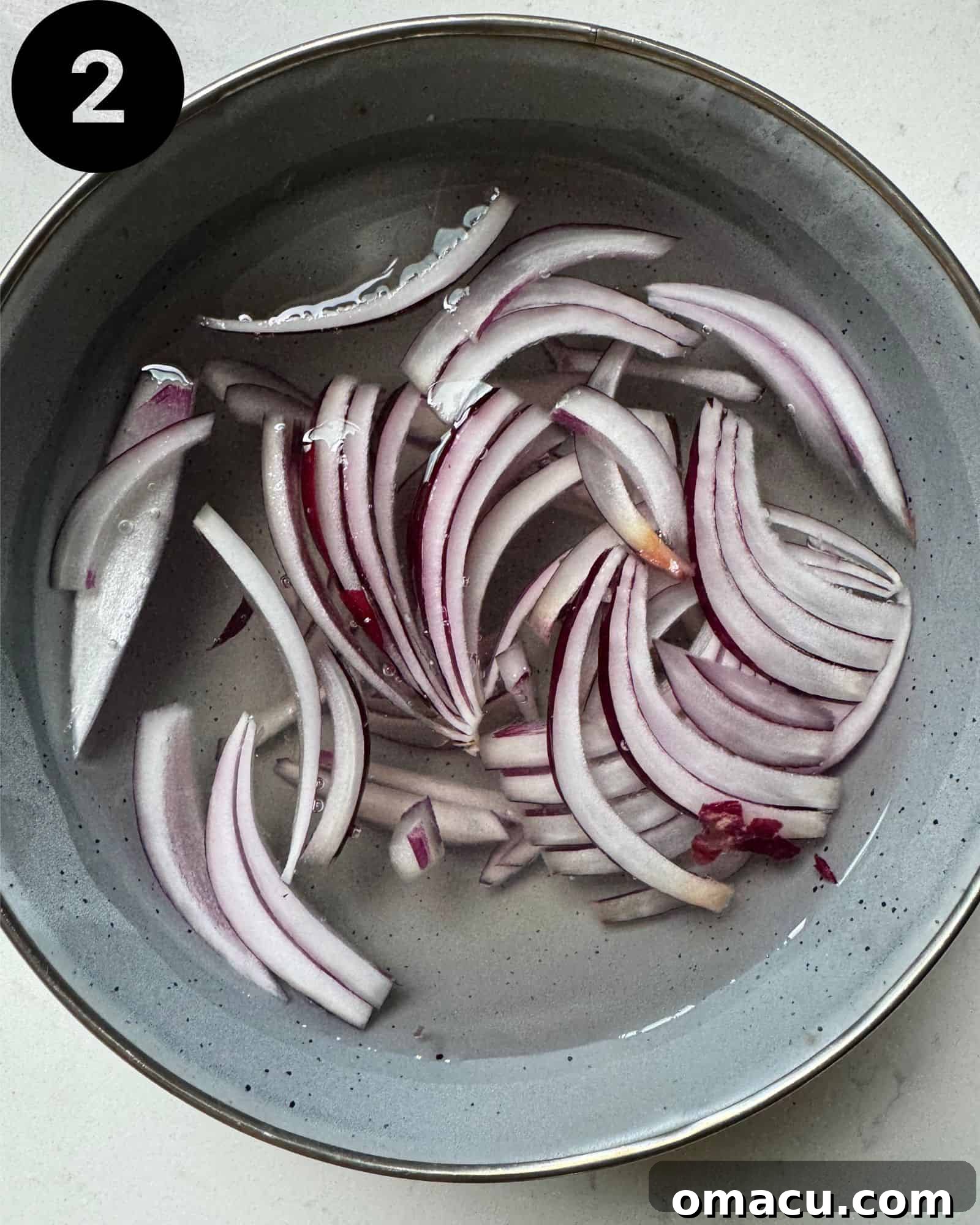Finely sliced red onion submerged in a small bowl of ice water, a preparation step to reduce its strong flavor, ready for salad assembly.