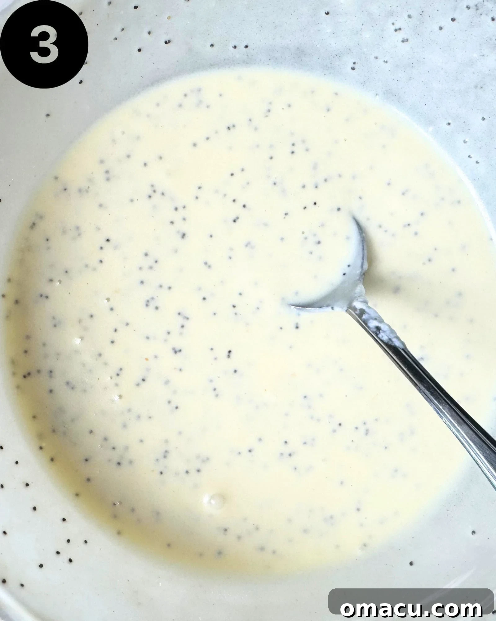 A rich, creamy homemade poppyseed dressing whisked to perfection in a glass bowl, with a spoon resting inside, ready to elevate any salad.