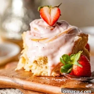 A beautifully glazed strawberry cinnamon roll on a brown cutting board, accented with fresh strawberries.
