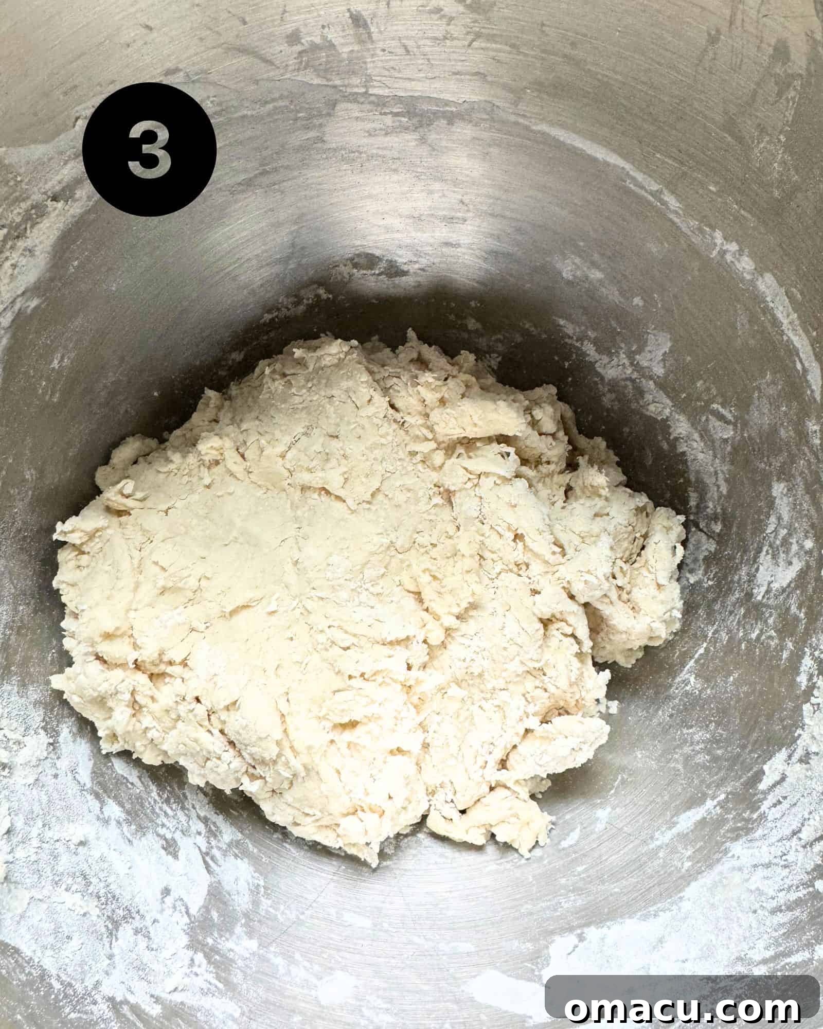 A shaggy, unrefined dough mixture in a stand mixer bowl, indicating the initial stage of dough formation for strawberry cinnamon rolls.