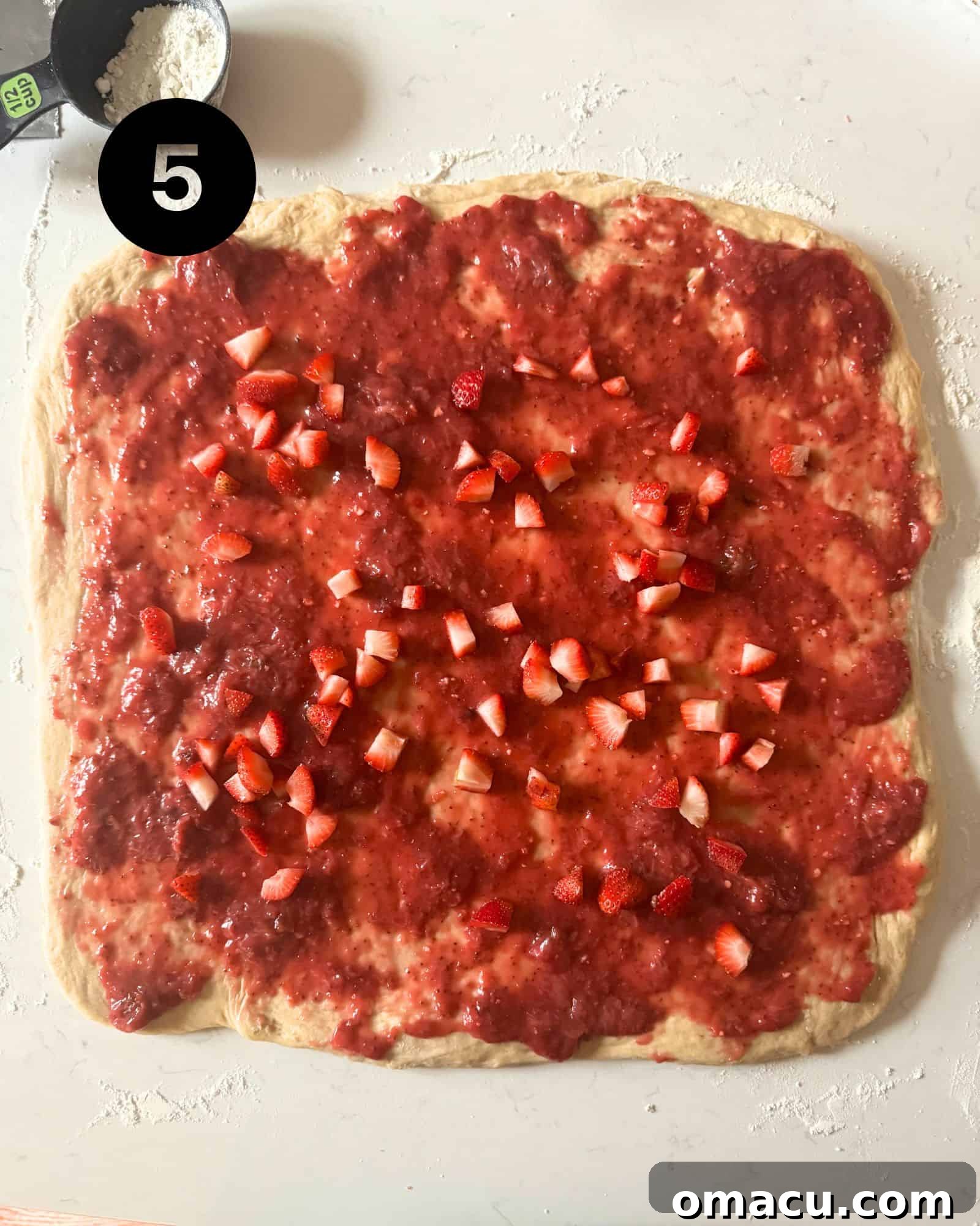Sweet strawberry filling beautifully spread across the cinnamon roll dough, preparing it for rolling and shaping.