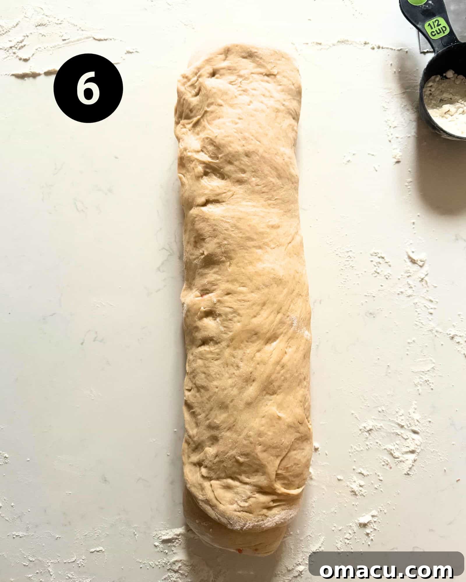 Cinnamon roll dough tightly rolled into a uniform log, ready to be cut into individual strawberry rolls.