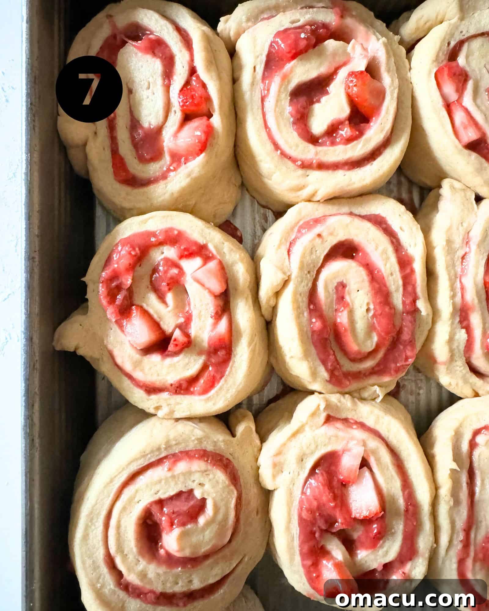 Freshly cut strawberry rolls neatly arranged in a baking dish, perfectly spaced for their second rise before baking.