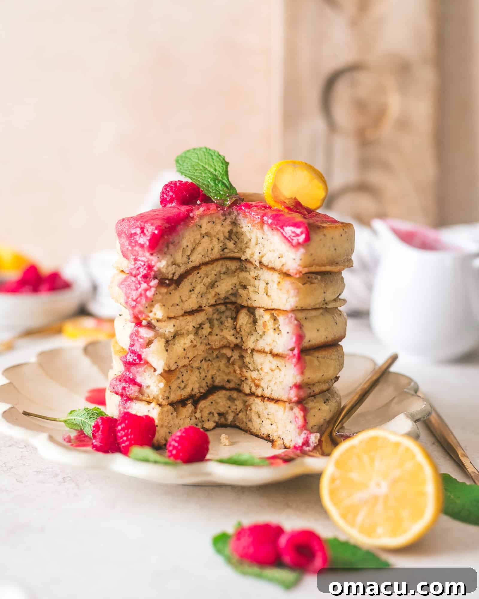 Stacked lemon poppy seed pancakes drizzled with raspberry coulis, garnished with fresh raspberries and lemon slices