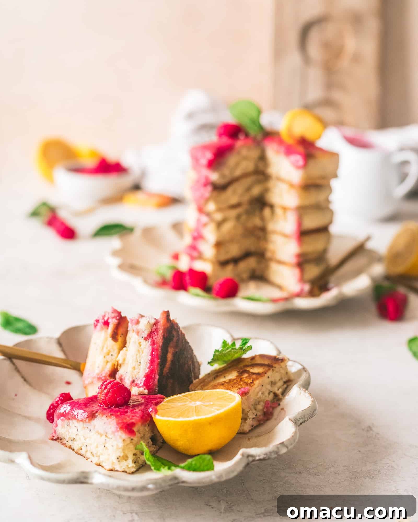 Close-up of lemon poppy seed pancakes on a white plate, topped with fresh raspberries and lemon slices