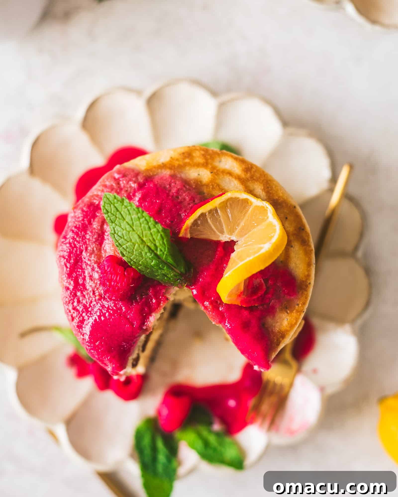 A stack of lemon poppy seed pancakes adorned with a drizzle of raspberry coulis and fresh fruit